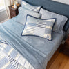 Bed with blue sheets and striped quilt and pillow shams a bedroom setting 