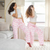 Two women wearing pink pajama pants with dogs and cake patterns in a living room.