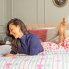 Woman lying on a bed with colorful bedding and pillows in a cozy bedroom.