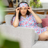 Woman in floral pajamas and eye mask sitting on a couch in a home setting
