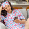 Woman in floral pajamas and eye mask using a phone on a couch