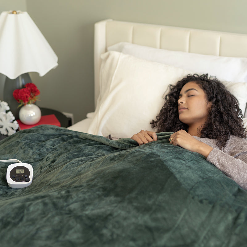 Woman sleeping under a green blanket with a digital controller next to her on a bed.