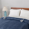 Blue heated blanket on a bed with white pillows and a lamp in the background