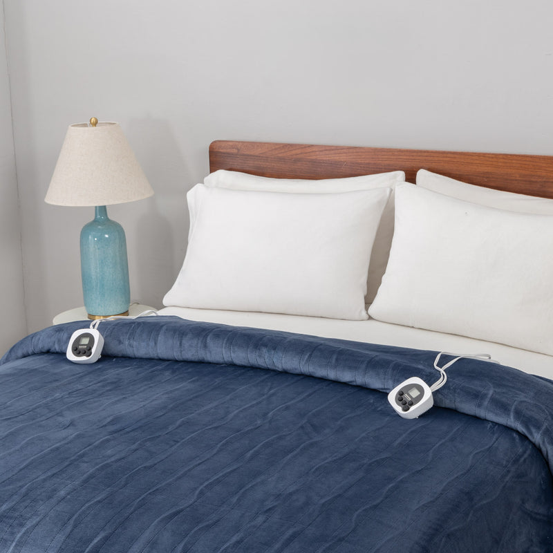 Blue heated blanket on a bed with white pillows and a lamp in the background