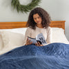 A woman sitting on a bed with a blue heated blanket.