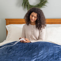 A woman sitting on a bed with a blue heated blanket.