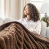 Woman sitting on a couch with a brown blanket, smiling.