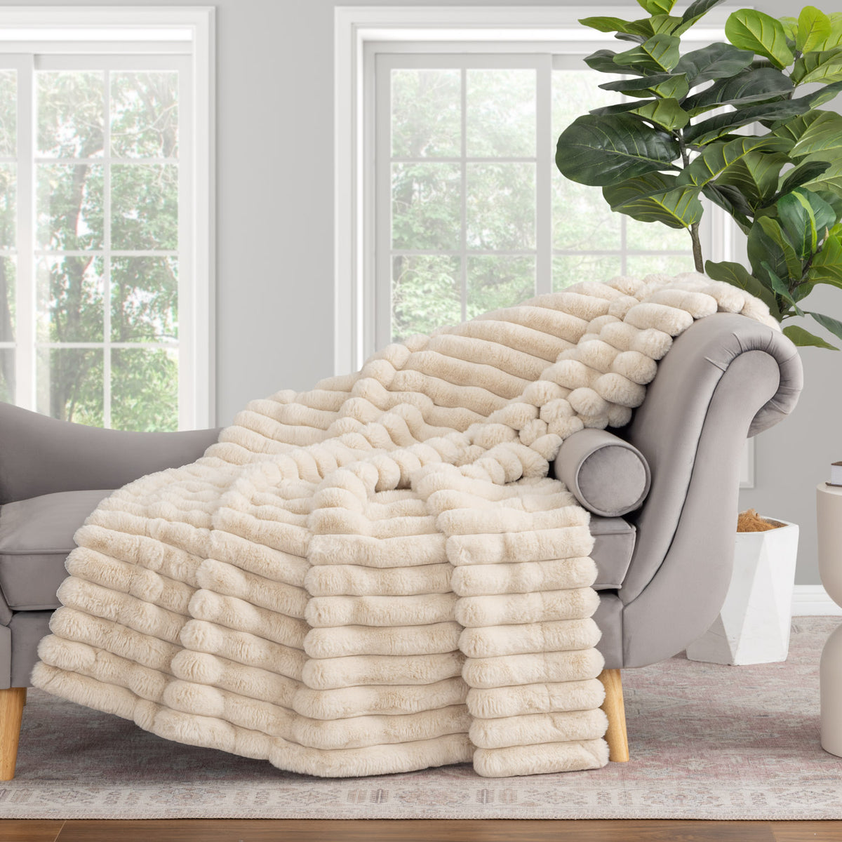 Beige blanket draped over a gray armchair in a room with large windows and a plant.