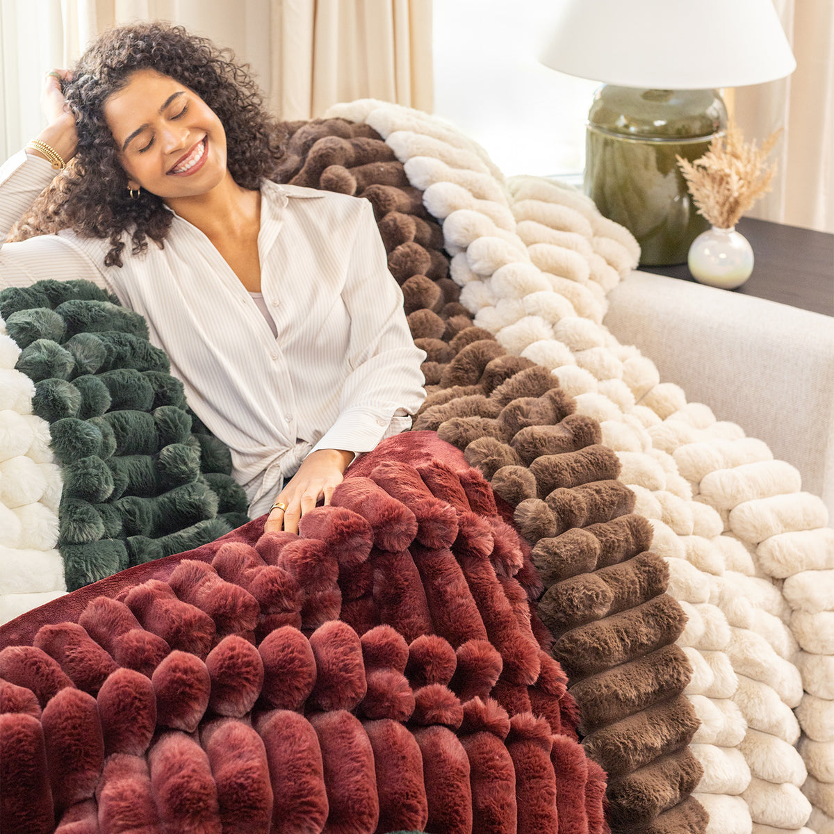Woman sitting on a couch with a pile of colorful textured blankets.
