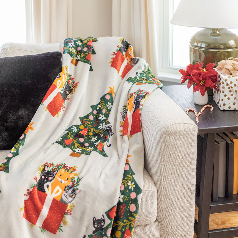 Cat printed holiday throw draped over a beige sofa.