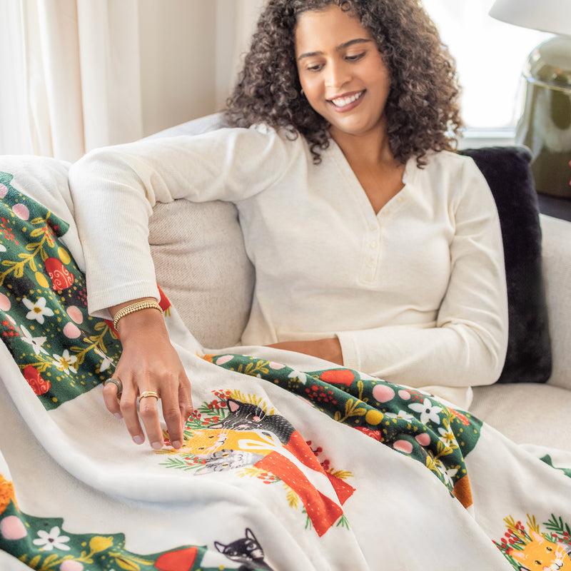 A woman sitting with a cat printed holiday throw draped over a beige sofa.