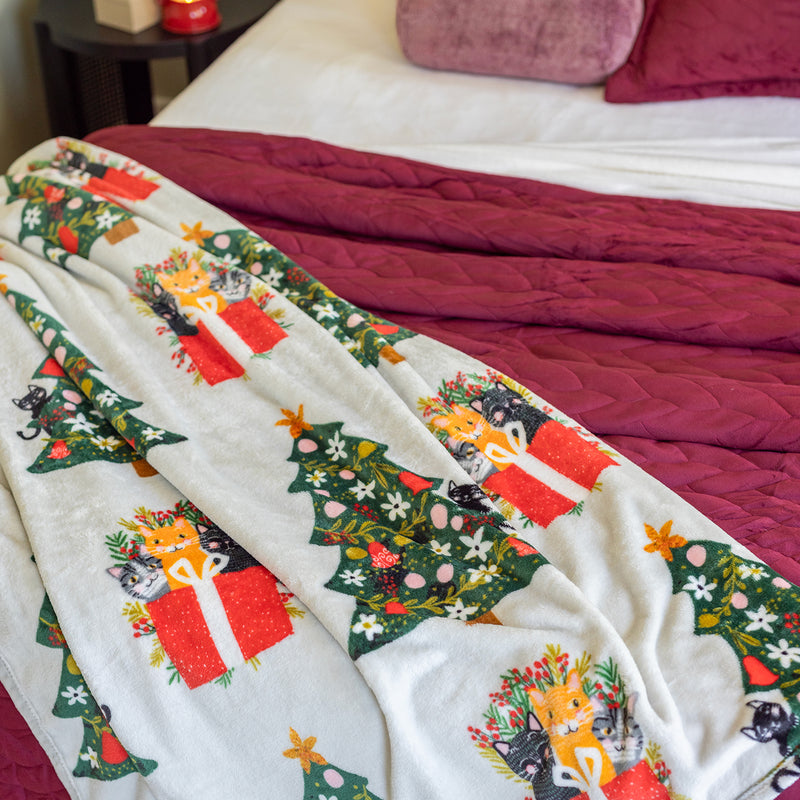 Cat printed holiday throw draped over a bed.