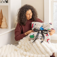 A woman sitting on a chair with a  snoopy holiday throw wrapped in a bow.