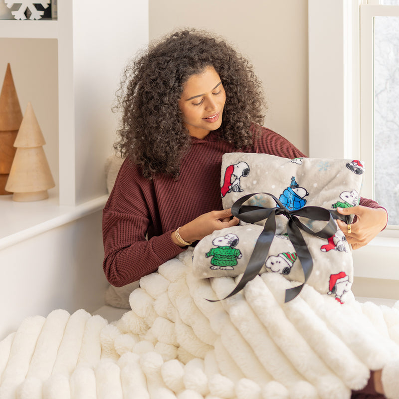 A woman sitting on a chair with a  snoopy holiday throw wrapped in a bow.