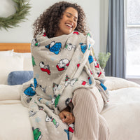 A woman sitting on a bed with a  snoopy holiday throw.