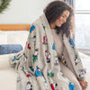 A woman sitting on a bed with a  snoopy holiday throw draped over her shoulders.