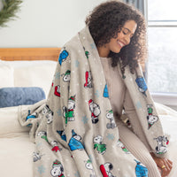 A woman sitting on a bed with a  snoopy holiday throw draped over her shoulders.