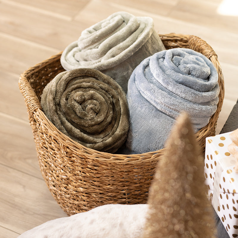 A bundle of blue, gree, and beige VelvetLoft Throws rolled up in a woven basket.