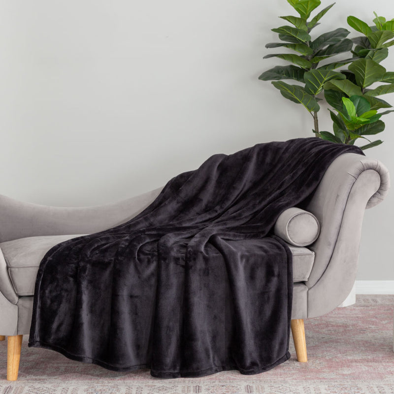 A black velvety plush throw draped neatly over te arm of a light grey chair.