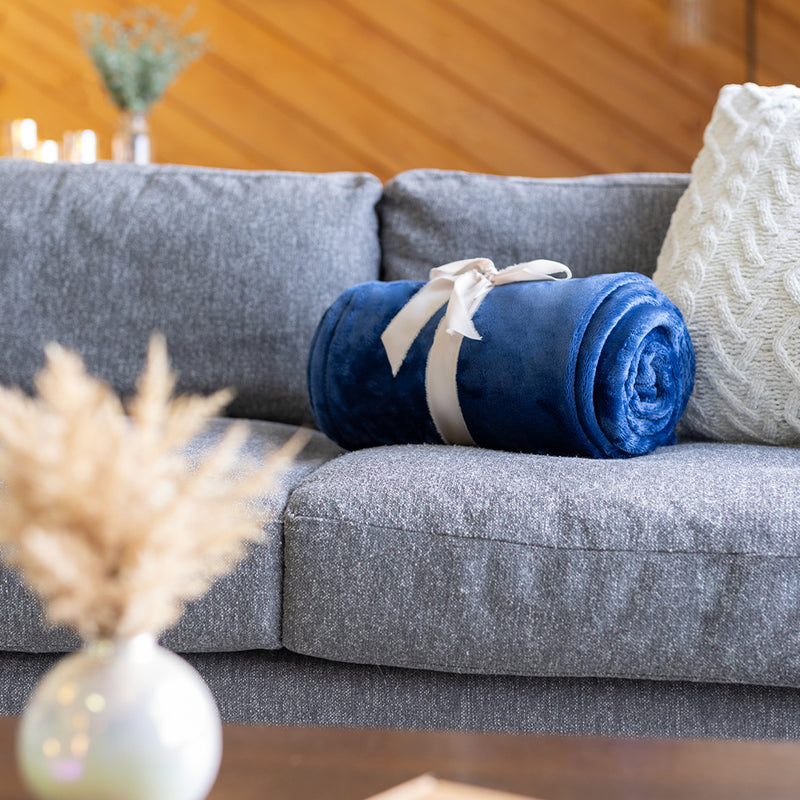 Our rolled blue VelvetLoft Throw tied in a bow laying on a grey sofa.