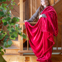 A woman standing next to a wooden staircase with a neon red velvety throw draped over her shoulder as she smiles.