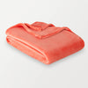 A neon orange velvety throw folded neatly on a white surface.