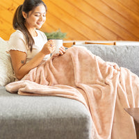 Our Hushed Auburn VelvetLoft Throw draped over a woman's legs as she holds a mug of coffee and sits on a grey couch.