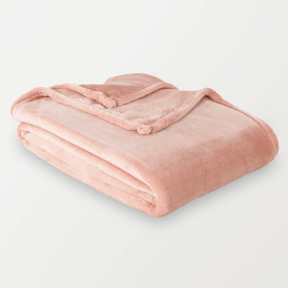 A blush pink velvety throw folded neatly on a white surface.