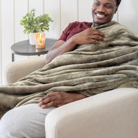 A man sitting on a beige cough with our Kalamata colored VelvetLoft Throw draped over his left shoulder.