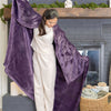 A purple velvety plush throw draped over a womans shoulders as she stands in front of a fireplace.