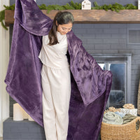 A purple velvety plush throw draped over a womans shoulders as she stands in front of a fireplace.