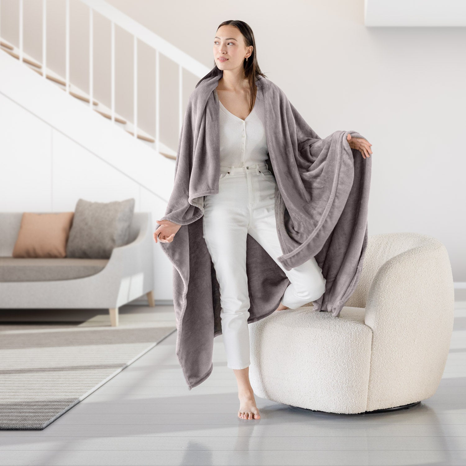 Woman in a gray cardigan and white pants standing in a modern living room.