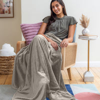 Woman sitting on a chair with a gray blanket draped over her, in a cozy living room setting.