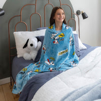 Person sitting on a bed wearing a blue Snoopy-themed blanket
