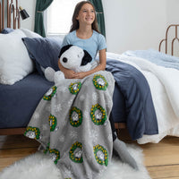 Girl sitting on a bed holding a stuffed dog under a Snoopy blanket with wreath pattern