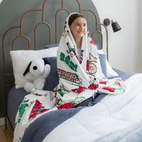 Person sitting on a bed with a colorful blanket, surrounded by pillows and a stuffed dog toy.