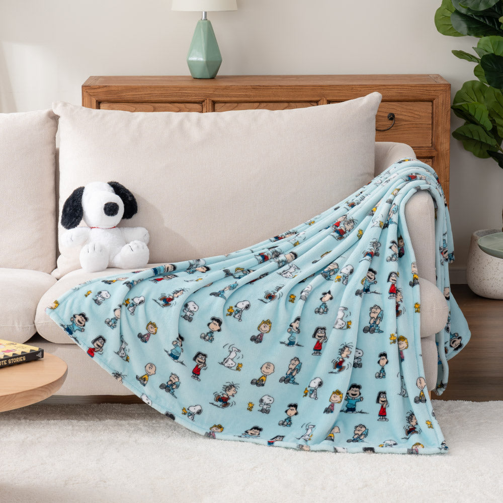 A light blue throw blanket featuring Peanuts characters draped over a chair with a plush toy beside it.