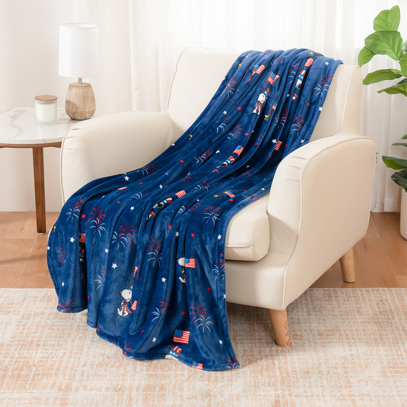 A cobalt blue Peanuts flag parade throw draped neatly over a beige leather chair.