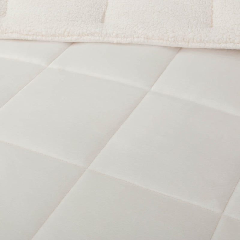 A close-up of a white quilted comforter showing its stitching and plush texture.