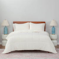 A white quilted comforter draped over a bed with white pillows and blue lamps on both sides.