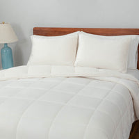 A white quilted comforter draped over a bed with matching white pillows.