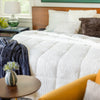 A white quilted comforter neatly spread on a bed with a navy throw and decorative pillows.