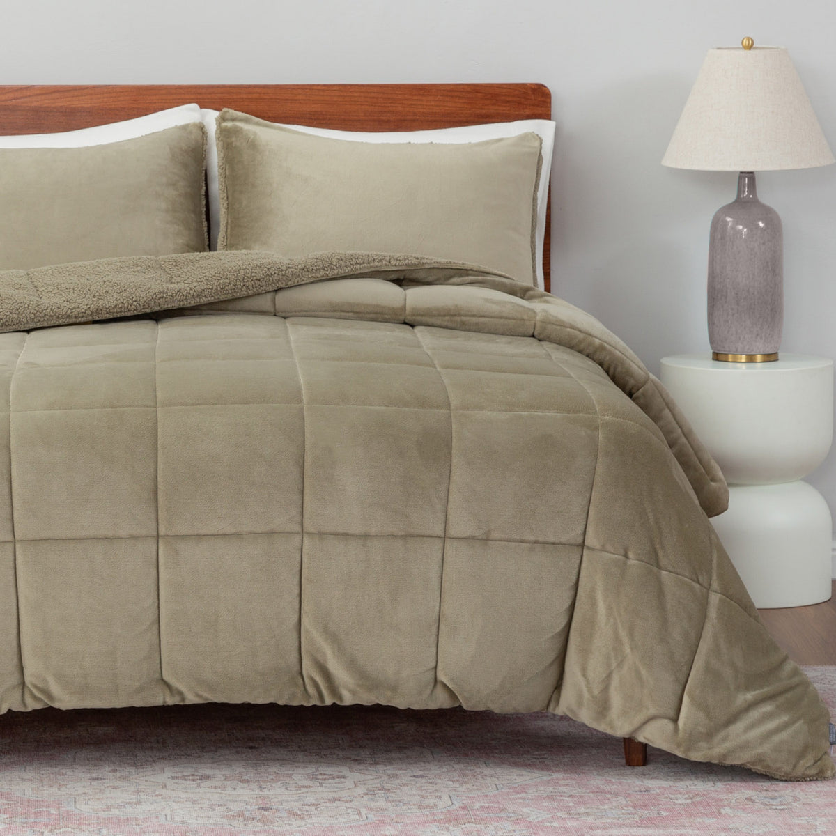 Beige comforter set on a bed with pillows and a lamp in the background