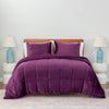 A purple quilted comforter draped over a bed with matching purple pillows and a decorative throw.