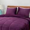 A purple quilted comforter draped over a bed with matching purple pillows.