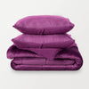 A stack of a purple quilted comforter neatly folded on a white background.