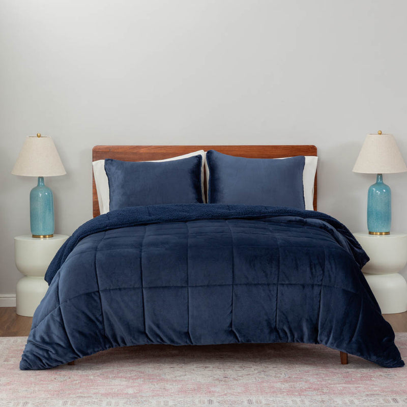 A navy quilted comforter draped over a bed with matching navy pillows and blue lamps on both sides.