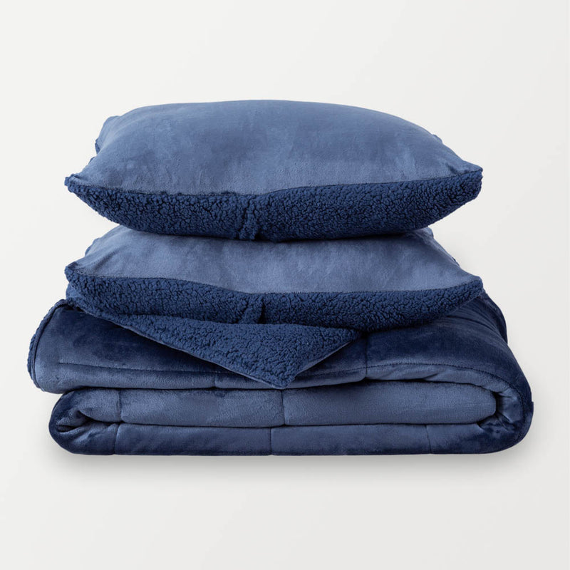 A folded navy quilted comforter displayed on a white surface.