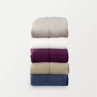 Five folded comforters in grey, white, beige, navy, and purple stacked vertically on a white background.