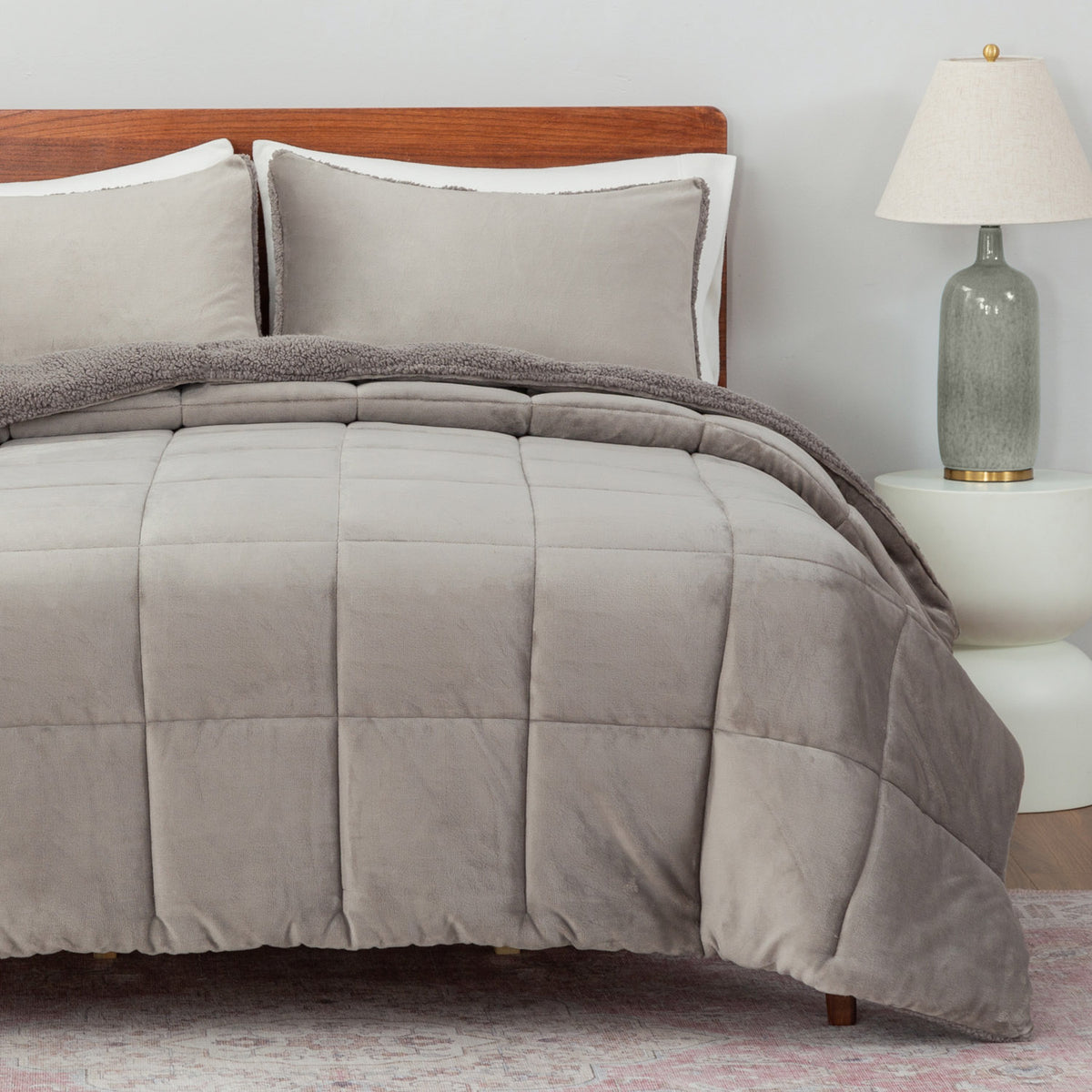Gray comforter set on a bed with pillows and a lamp in the background